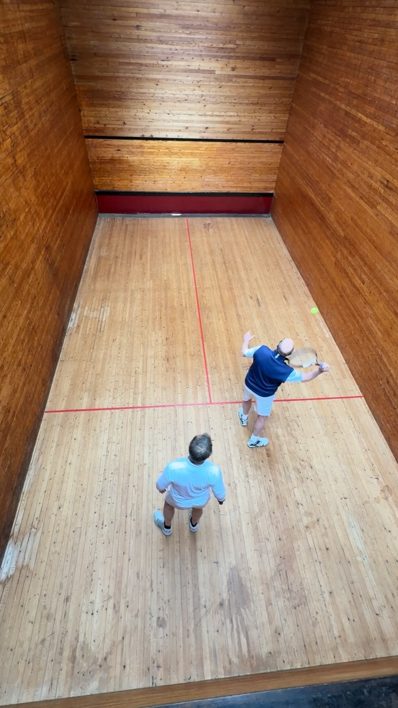 Gary Squires, in blue, serving in the Moreton Morrell squash tennis court, seen from the gallery