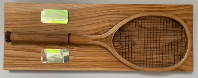 A squash tennis racket from about 1920, mounted on a wooden board with two brass plaques